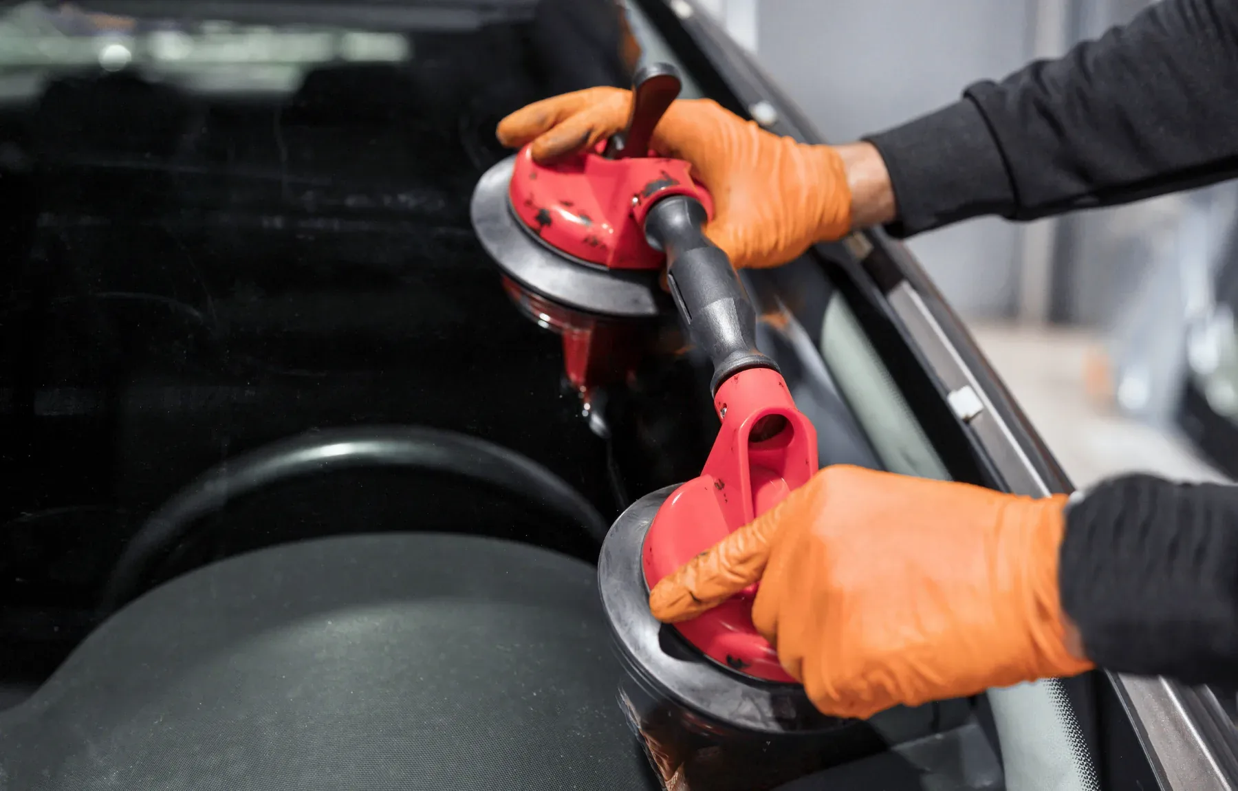 A close-up, high-angle shot shows a person's hands in orange rubber gloves gripping two red pistol-grip suction-cup tools mou