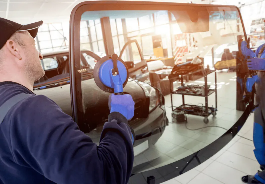 Technician in blue gloves holding a suction cup tool while working on a vehicle window at an auto glass repair shop.