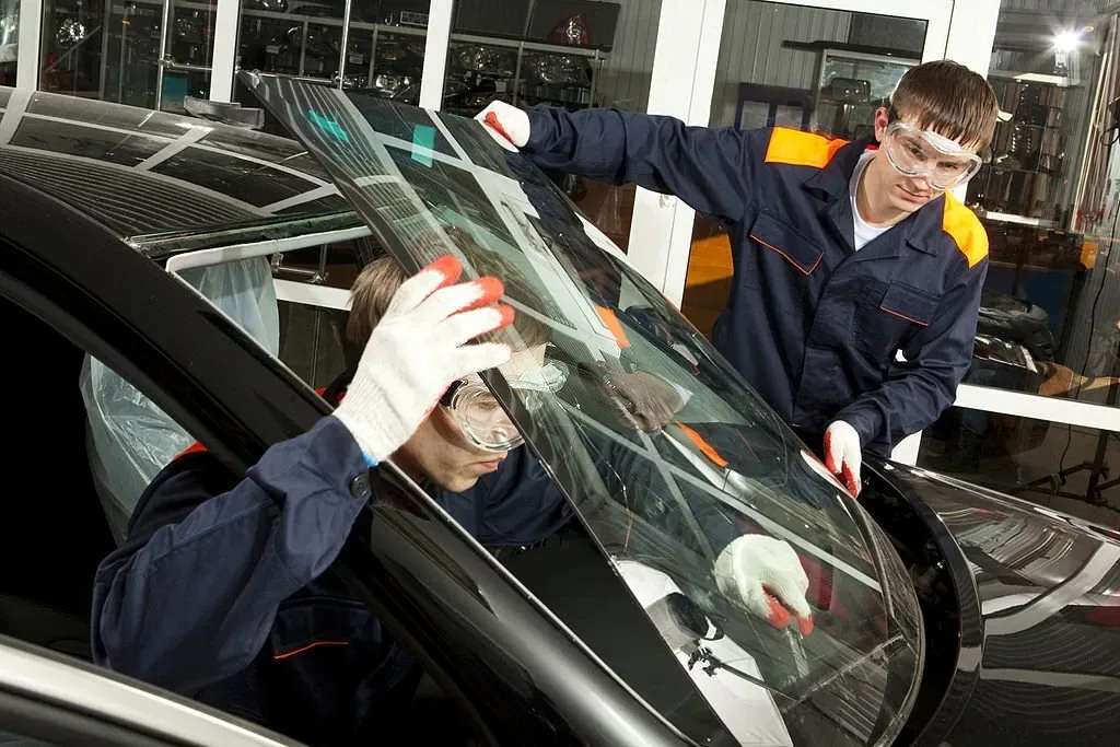 Two auto glass technicians installing a windshield on a vehicle at an auto glass repair shop.